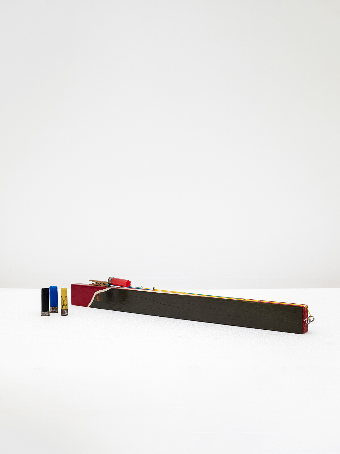 Kids Rifle, 2024, Painted wood, strings, used hunting cartridges, 67 x 3.5 x 5.5 cm